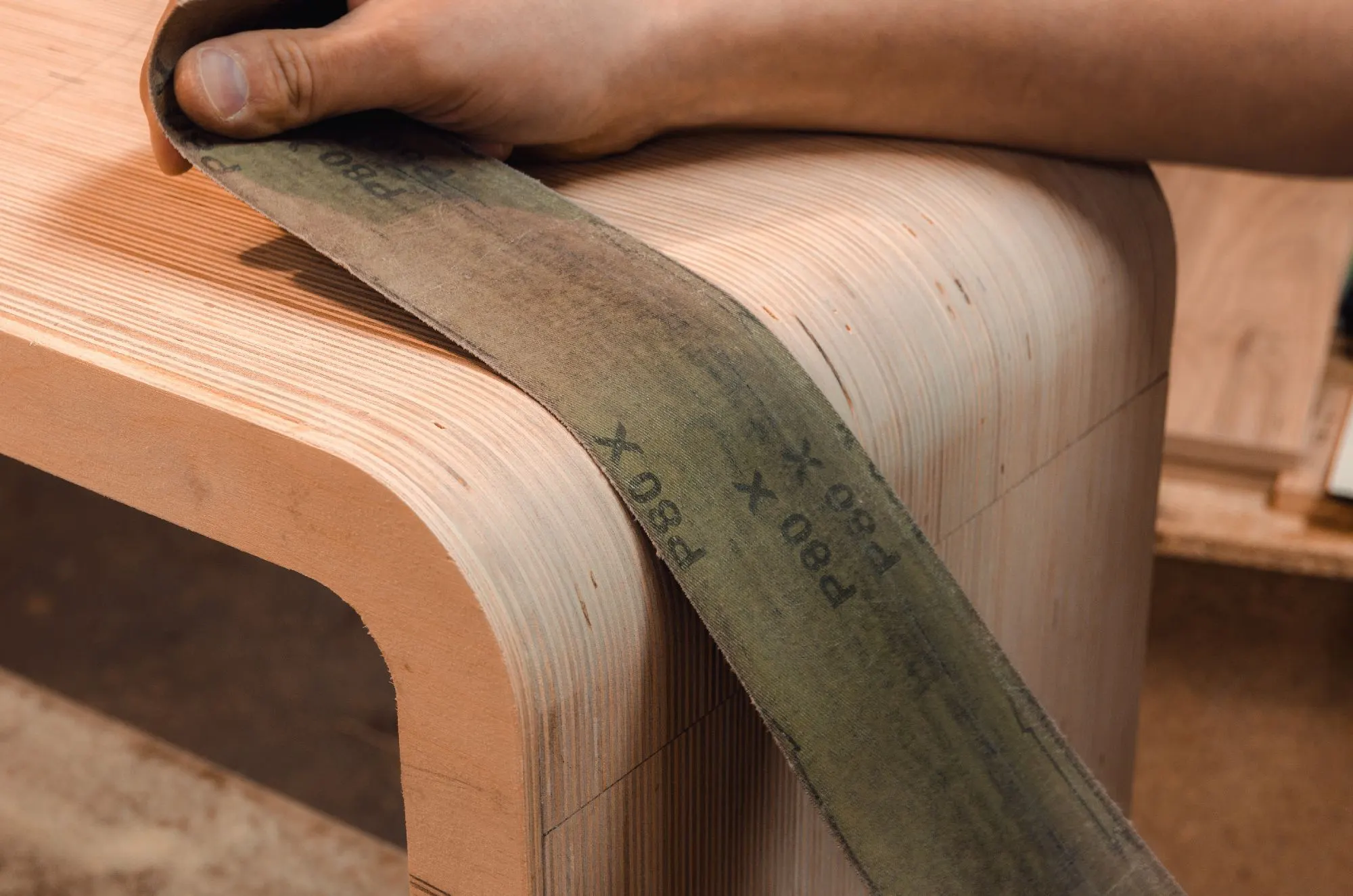 Hand schleift mit Schleifband die gerundete Kante eines Holzmöbels